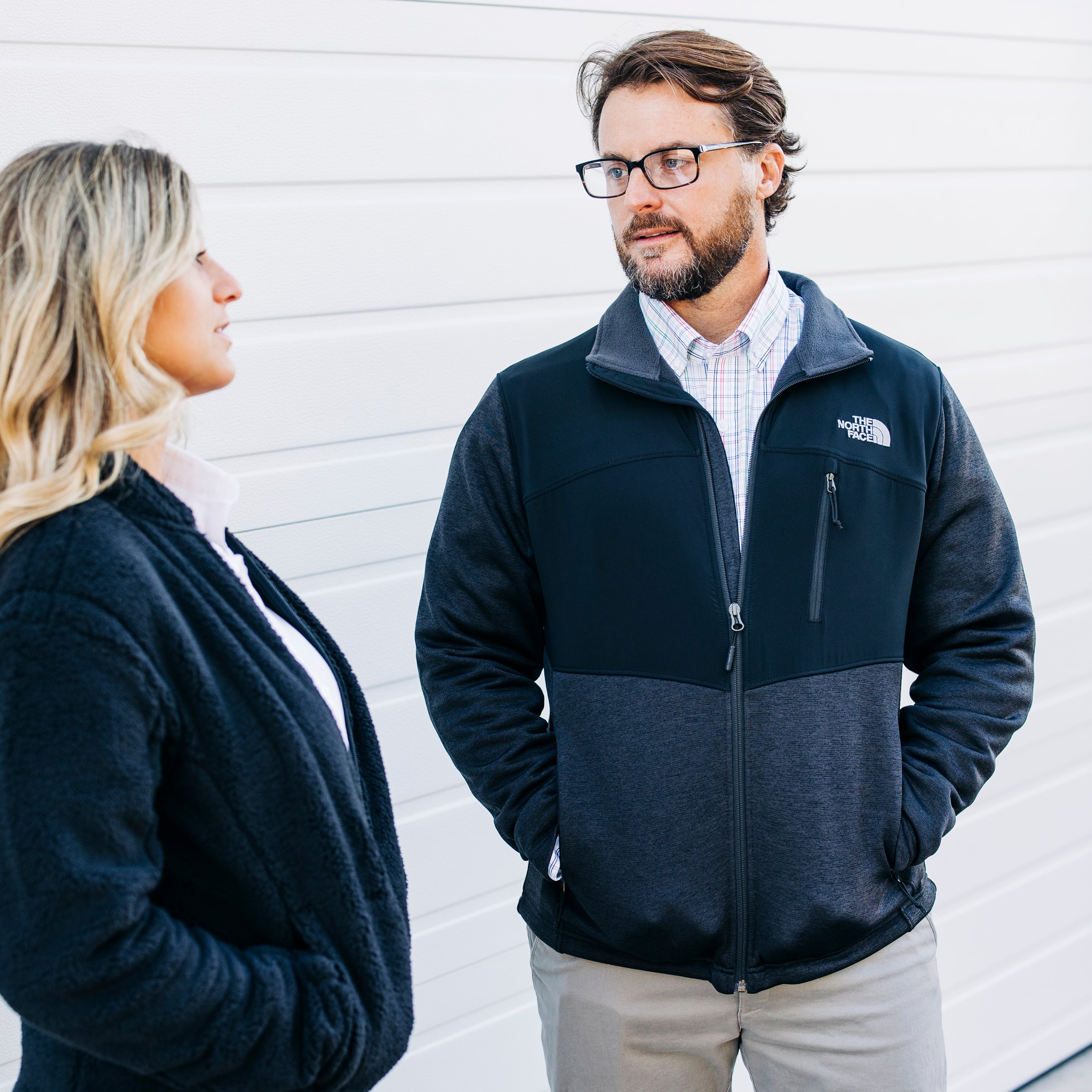 Man wearing The North Face jacket from Port City Apparel speaking to a woman in a black jacket from Port City Apparel.
